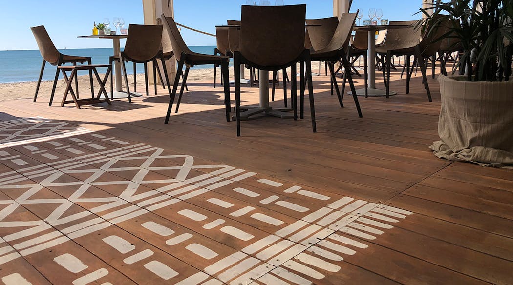 Un motif représentant un tapis d'inspiration berbère peint sur une terrasse en bois face à la mer