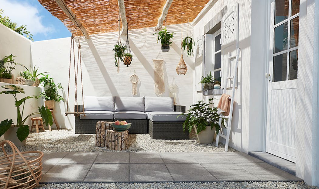 Une terrasse bohème avec des plantes suspendue et un sol en gravier et dalles béton