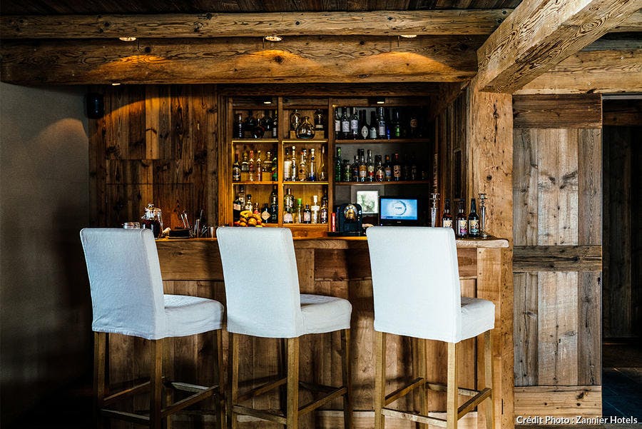 Bar totalement en bois avec trois tabourets couverts de tissu blanc.