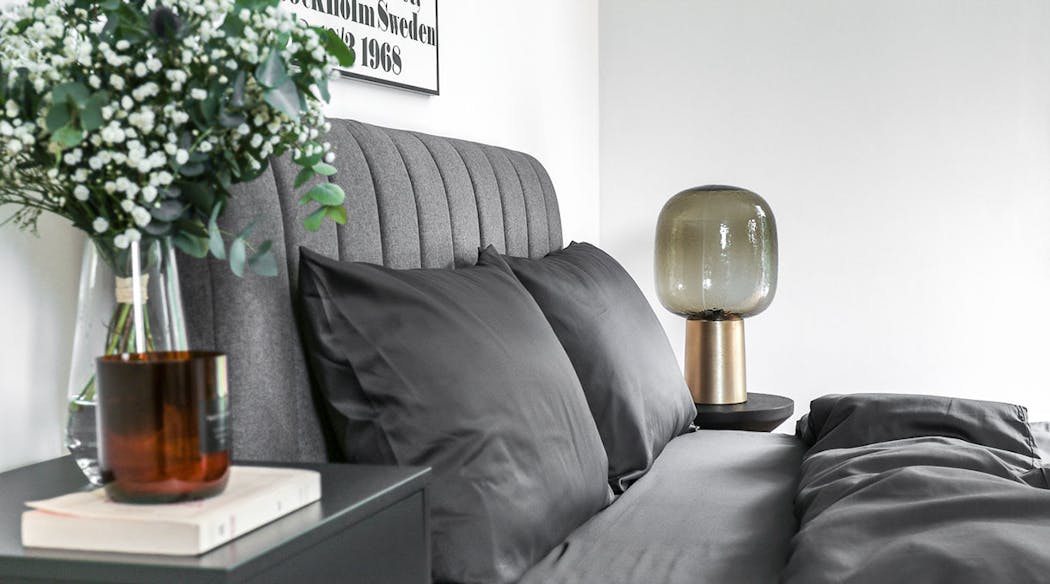 Un chambre design avec une tête de lit matelassée et des draps gris, une lampe en verre fumé et laiton