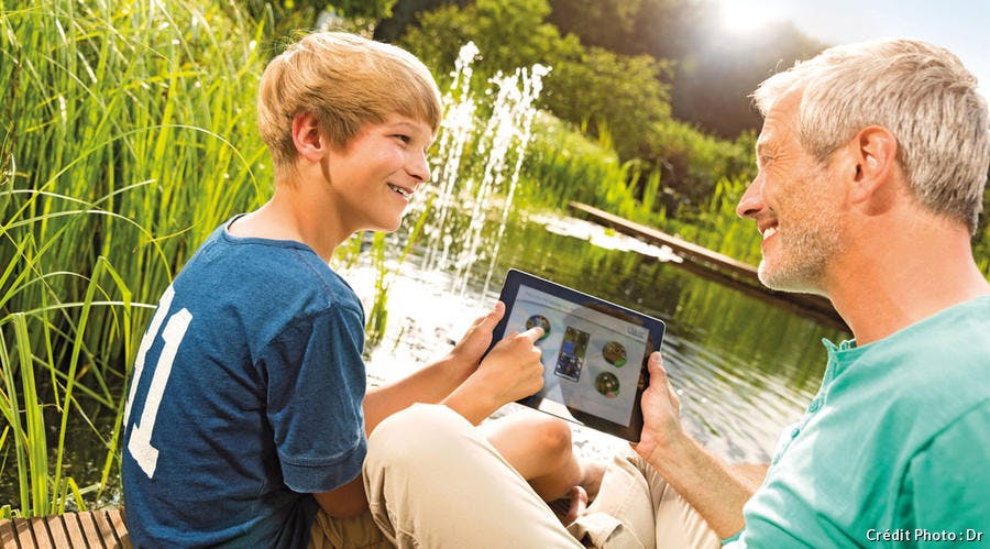 un père et un fils qui sourient en regardant une tablette face à un bassin