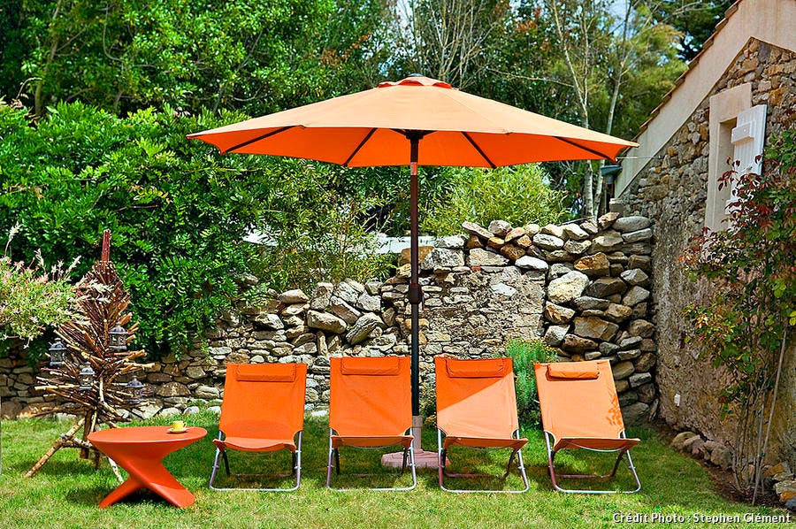 Transats oranges sous parasol dans un jardin ensoleillé.