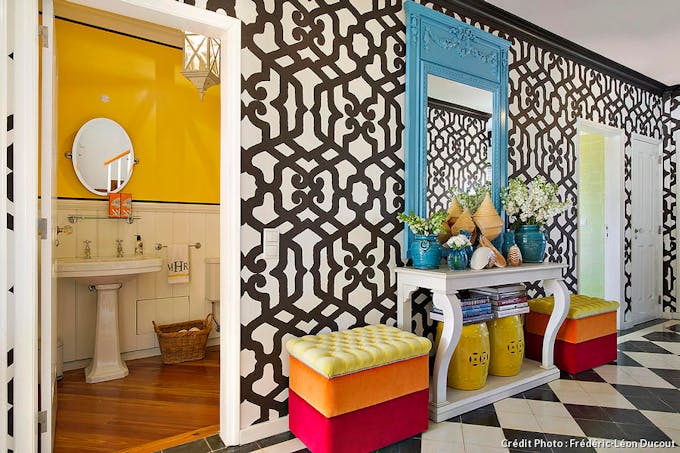 Entrée colorée pleine d'imprimés et de motifs sur les murs, donnant sur une salle de bain jaune.