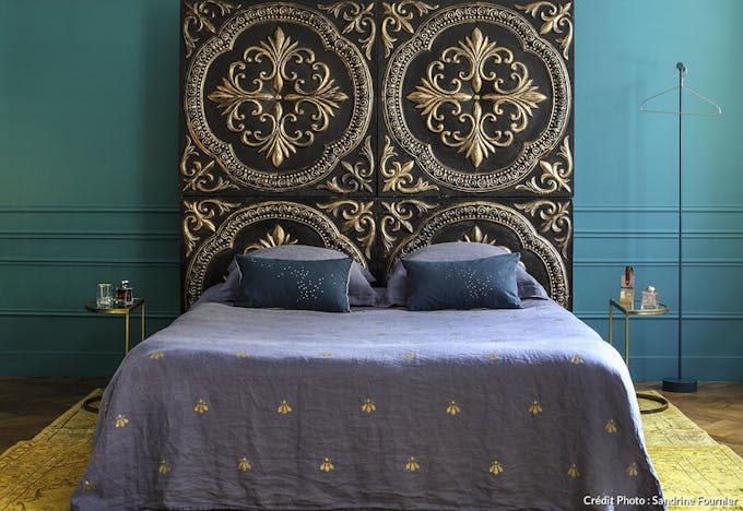 Chambre avec tissus et tête de lit doré aux motifs inspirés de la royauté.