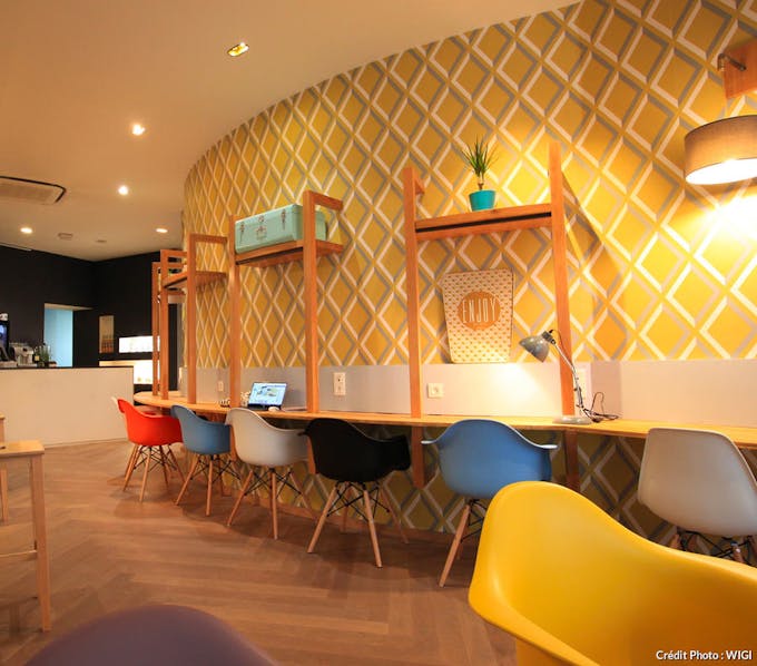 Une enfilade de bureaux face à un mur avec du papier peint vintage à motifs « losange »  dans des camaïeux de moutarde et de bleu délavé. 