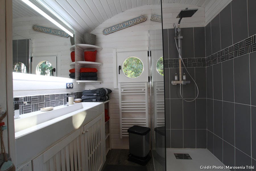 La salle de bain mixe les matériaux : carreaux de ciment façon ardoise dans la partie douche et lambris blancs pour une déco très graphique. Une double vasque. Une douche XXL.