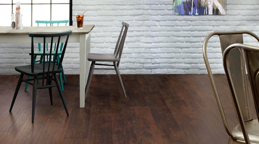 Une cuisine avec un mur de briques blanches et un sol en pvc imitation bois couleur chocolat. Une table et deux chaise.