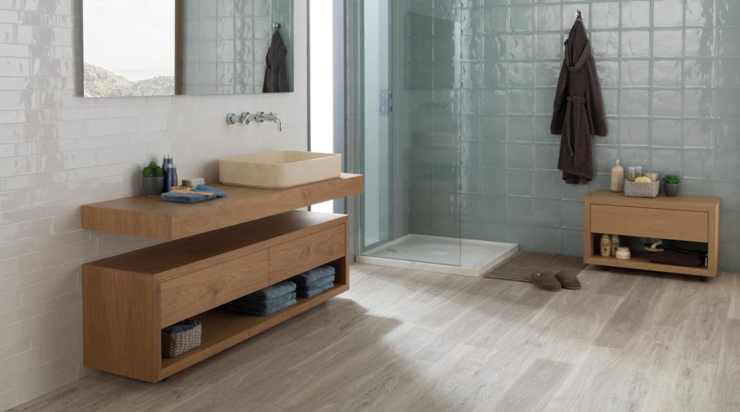 Une salle de bain moderne avec douche à l'italienne dans le fond et un bloc lavabo à gauche. Le sol imite le bois gris.