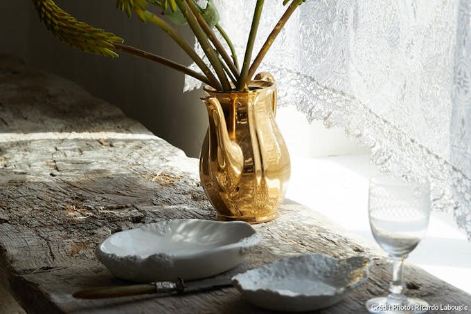 Vaisselle sur banc en bois et vase doré avec plante.