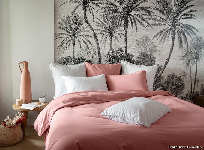 une chambre à coucher avec des draps roses et blanc et un papier peint noir et blanc à palmiers 