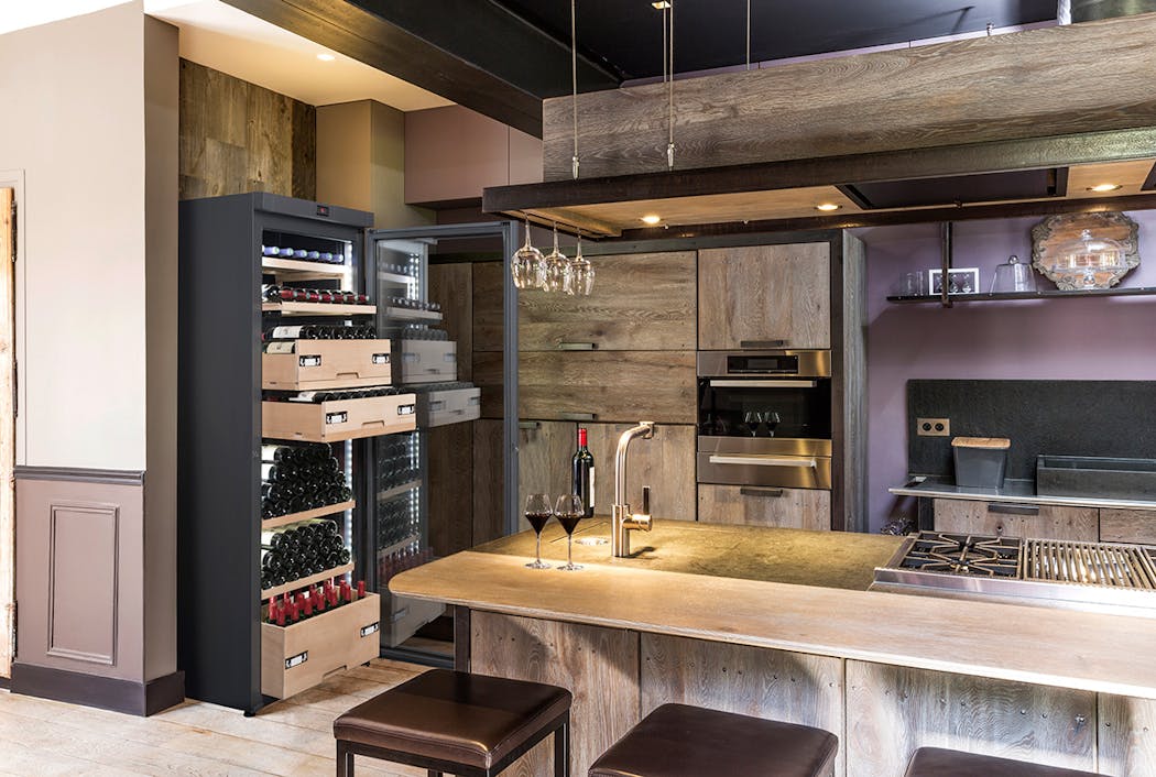 une cave à vin avec des clayettes en bois dans une cuisine familiale avec ilot central en bois/