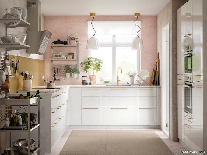 une cuisine blanche avec des poignées dorées et des murs roses