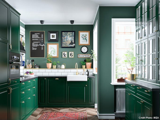 une cuisine avec des meubles vert sapin, une vasque blanche en céramique et des cadres accumulés en décoration