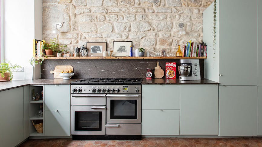 une cuisine vert d'eau avec piano de cuisson dans une cuisine avec pierres apparentes et tomettes
