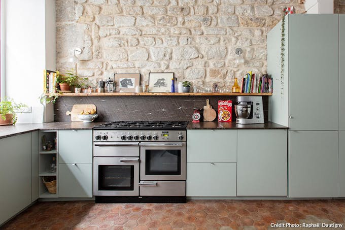 une cuisine vert d'eau avec piano de cuisson dans une cuisine avec pierres apparentes et tomettes