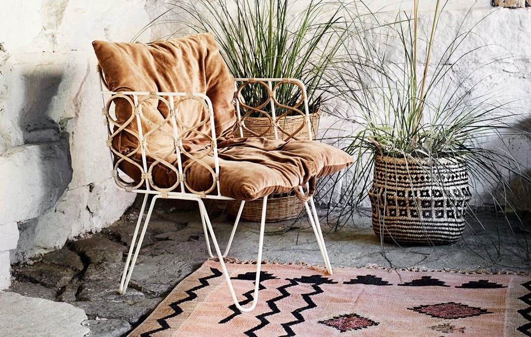 Un fauteuil de jardin vintage en métal avec un coussin et un tapis terracotta