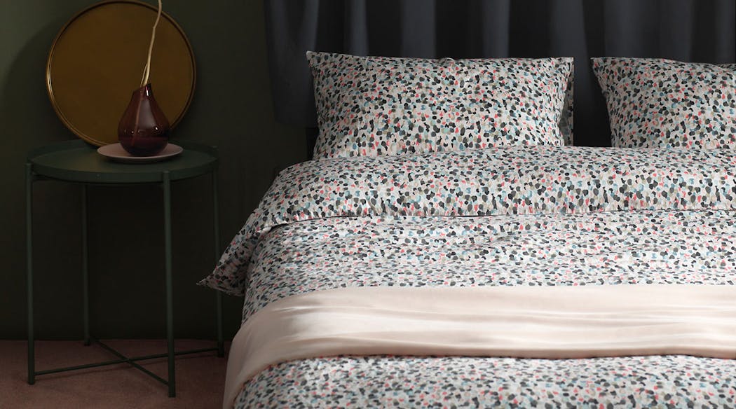 chambre à coucher avec table de chevet en métal vert et lit avec parure multicolores.