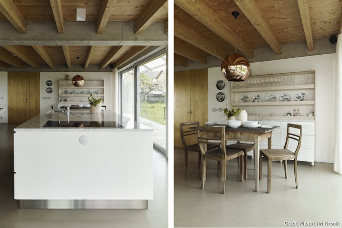 un cuisine ouverte avec un ilot central blanc et une salle à manger rustique avec un sol en béton et des poutres au plafond