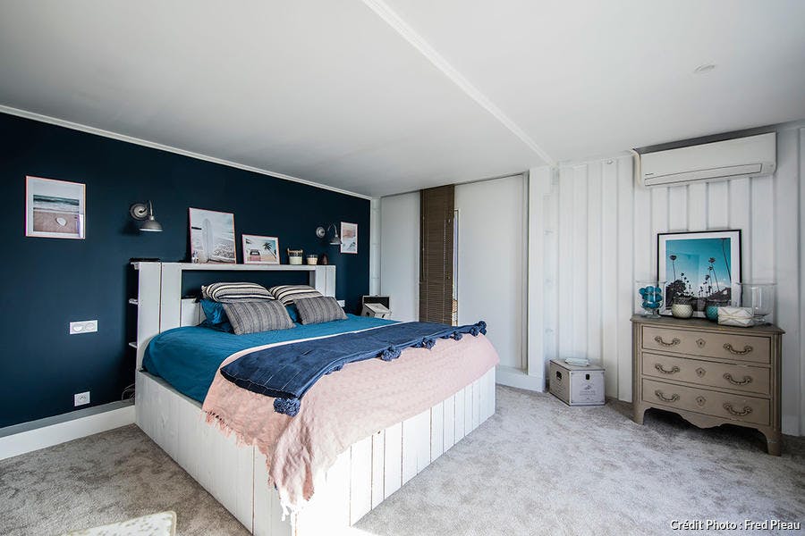 une chambre à coucher avec moquette et lambris, un lit en bois blanc et un mur bleu paon.