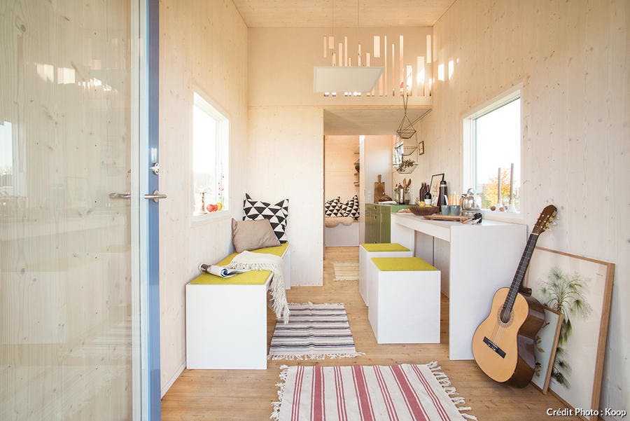 un salon chaleureux blanc et jaune avec cuisine ouverte et tapis rayés au sol