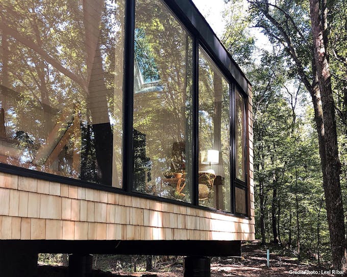 une cabane hygge dans la forêt avec de grandes baies vitrées