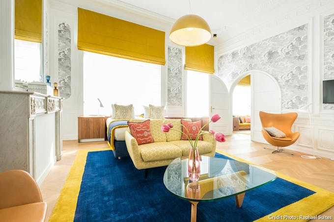 une salon avec moulure et hauteur sous plafond, réveillée par un tapis bleu et jaune avec un canapé coordonné et une table basse vintage
