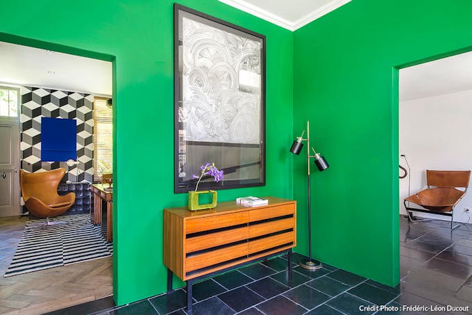 un couloir avec un mur vert vif, une commode vintage, un lampadaire industriel et une oeuvre d'art
