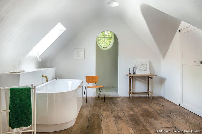 un salle de bains sous les toits avec parquet, baignoire en ilot et chaise vintage