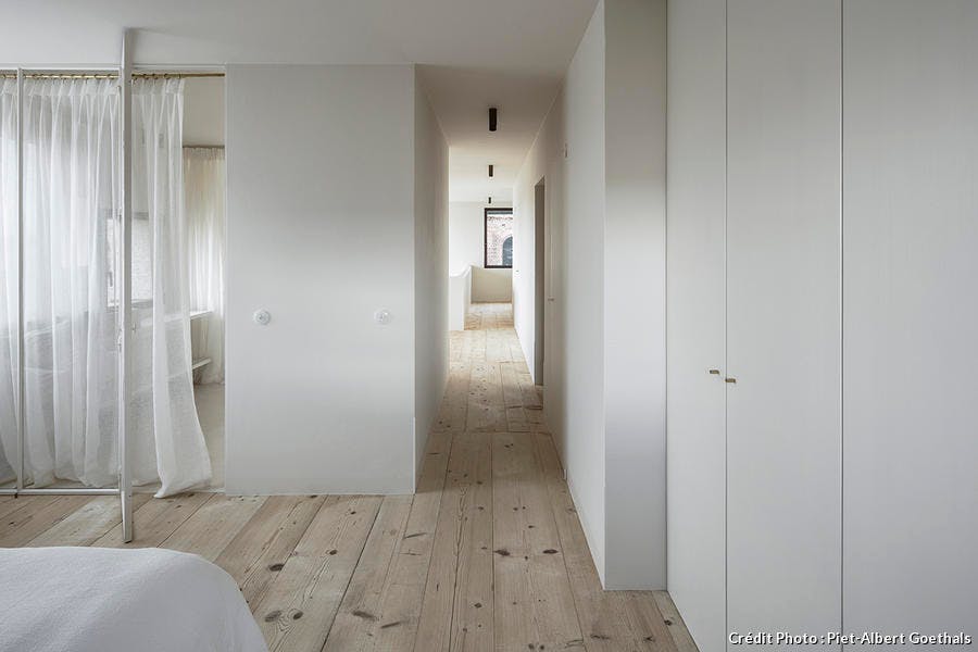 Une chambre minimaliste et épurée avec un sol en bois clair, des murs et des placards blanc intégrés