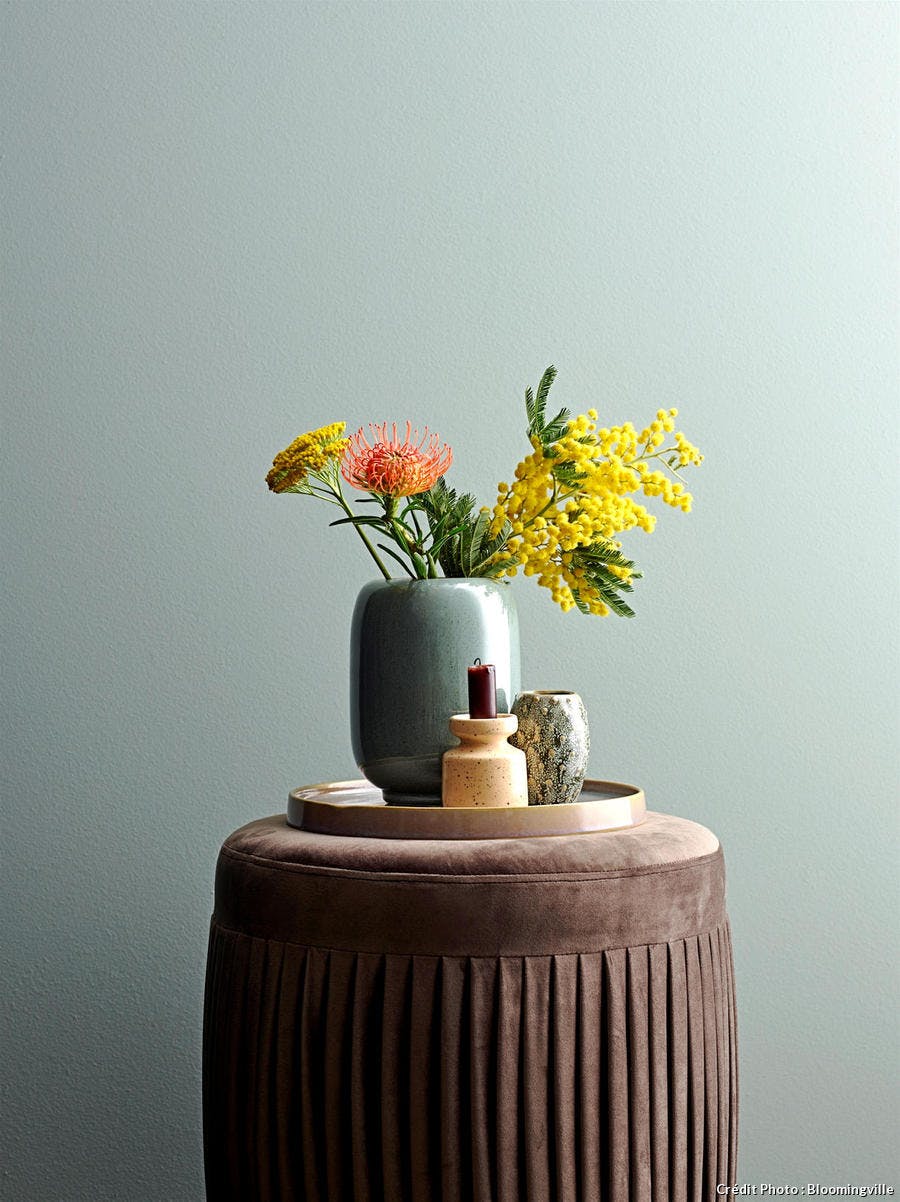 Un pouf rond en velours marron surmonté d'un vase avec des fleurs