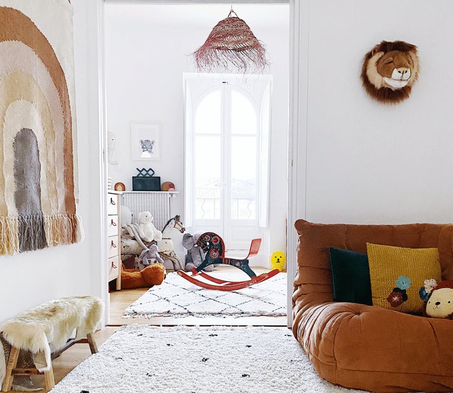 un salon lumineux avec un tapis berbère et un Togo en cuir marron donnant sur une chambre d'enfant.