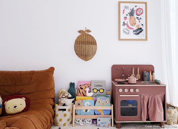 une chambre d'enfant avec un fauteuil Togo, une petite cuisine rose et une affiche multicolore.