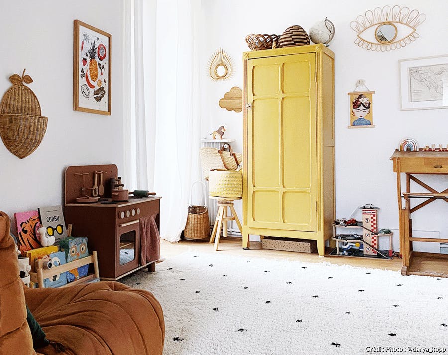 une chambre d'enfant avec un tapis berbère, une petite cuisine rose et une armoire d'écolier jaune.