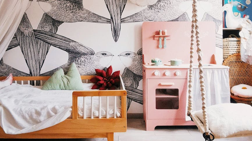 une chambre d'enfant avec un lit scandinave, une cuisinière en bois rose et un papier peint avec des oiseaux en noir et blanc