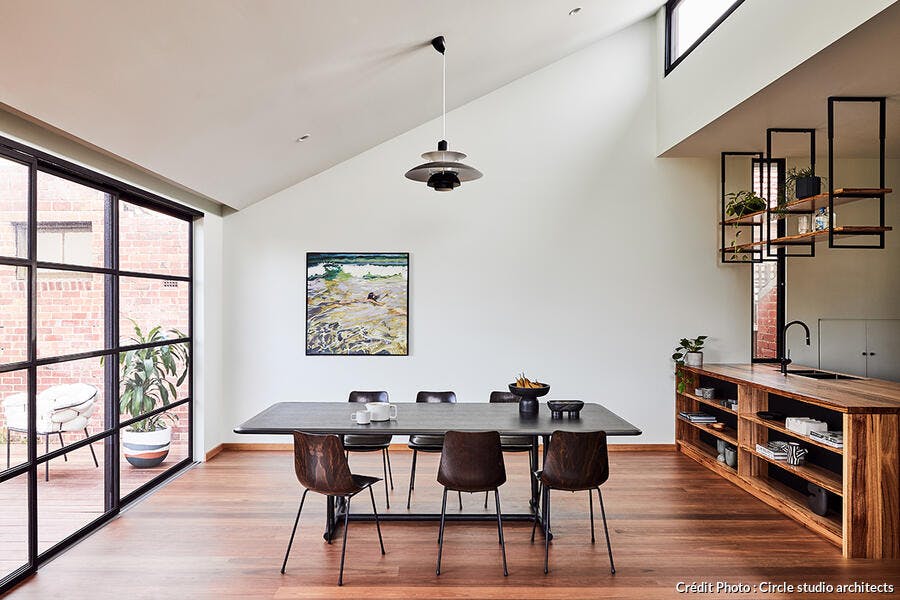 une pièce à vivre ouverte sur une cuisine dans une extension avec un parquet en bois chaud et ouvertures vitrées du sol au plafond