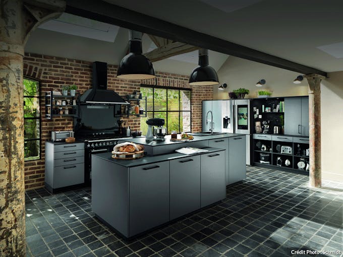 une cuisine noire matte avec des suspensions industrielles et un piano de cuisson