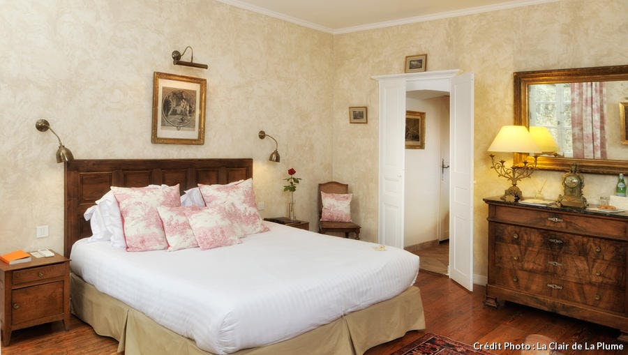 Une chambre aux tonalités très douces de paille avec des coussins en toile de jouy et des peintures encadrées aux murs.
