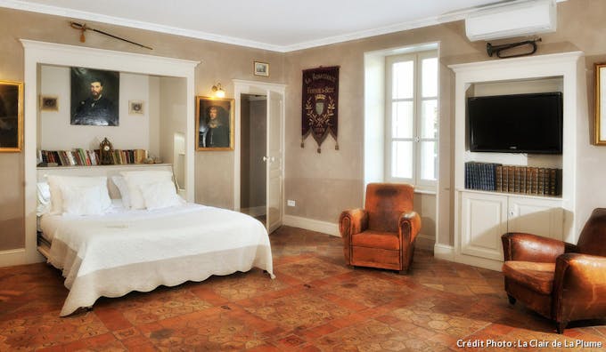 Une chambre avec un sol en tomettes anciennes et des peintures encadrées aux murs.