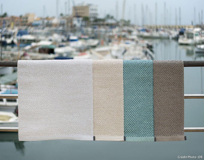 tapis d'extérieurs de différentes couleurs posés sur une rambarde avec vue sur un port