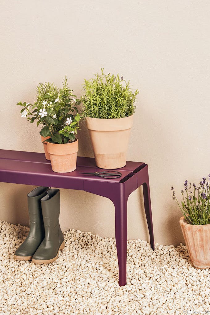 banc en métal de couleur aubergine avec en dessous des bottes en caoutchouc et au dessus des pots de plantes vertes