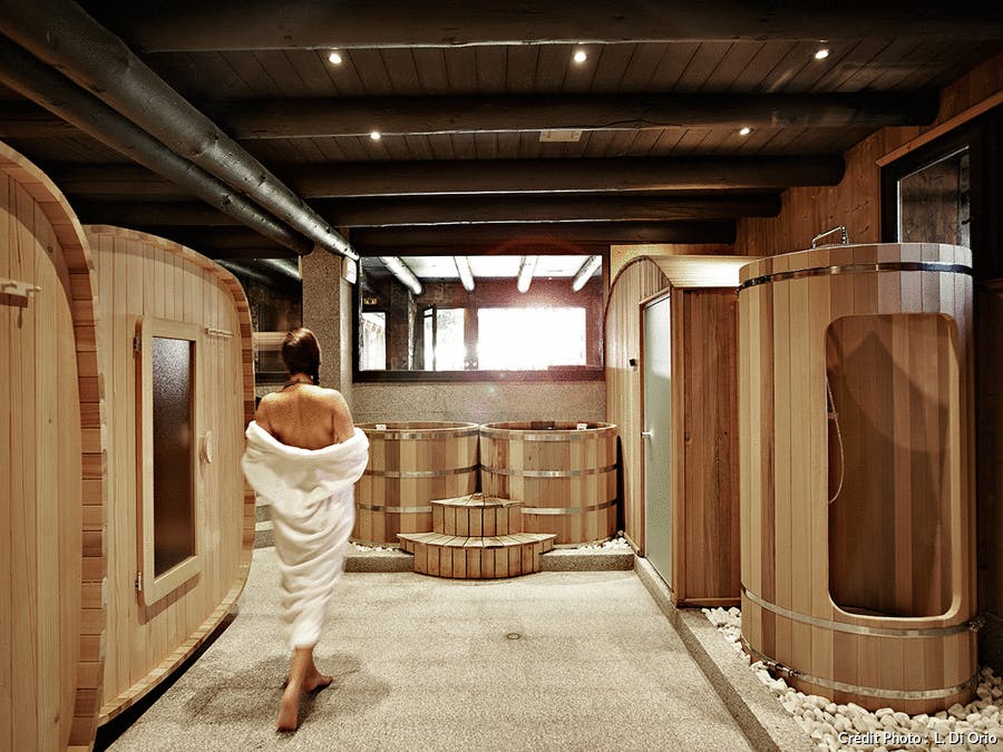 une femme en peignoir dans une salle avec des cabines hammam et sauna en bois clair 
