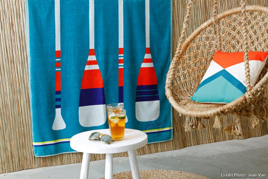 Une serviette Paddle bleue et un coussin Mirama Géométrique posé sur fauteuil hamac suspendu en fils de macramé.