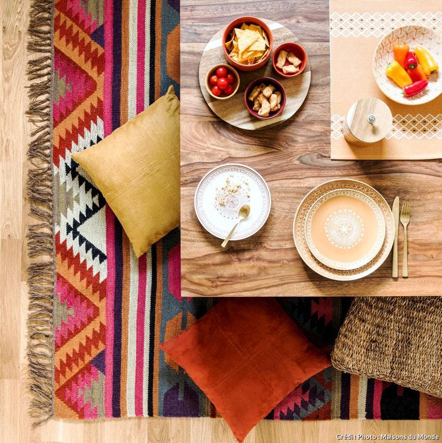 Table basse en bois, coussins colorés et tapis imprimé aztèque multicolore.