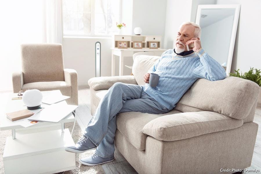 un sénior assis sur un canapé téléphone et boit un café