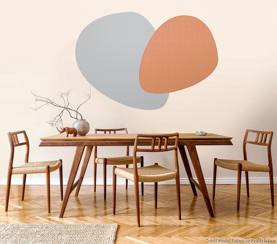 peintures murales aux motifs géométriques couleur brique et grise sur fond crème, table de salle a manger et chaises en bois