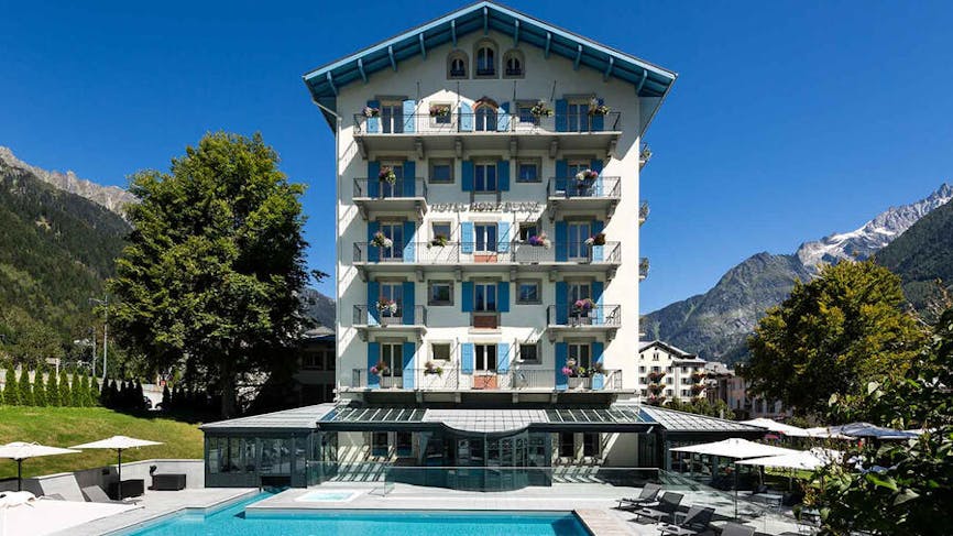 Vue d'ensemble de l'hôtel Mont-Blanc à Chamonix avec sa façade blanche et sa piscine turquoise face aux montagnes.