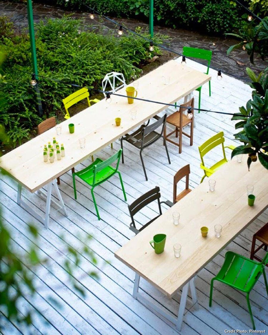 Terrasse style guinguette minimaliste avec table en bois façon étai et mix and match de chaises colorées