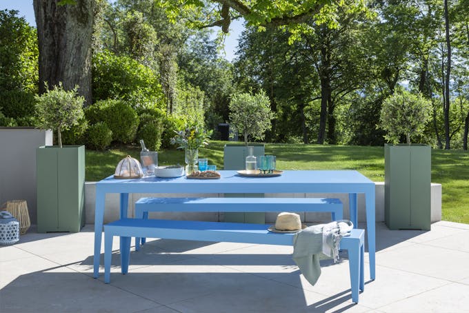 Bancs et table bleu sur une terrasse dans un jardin verdoyant