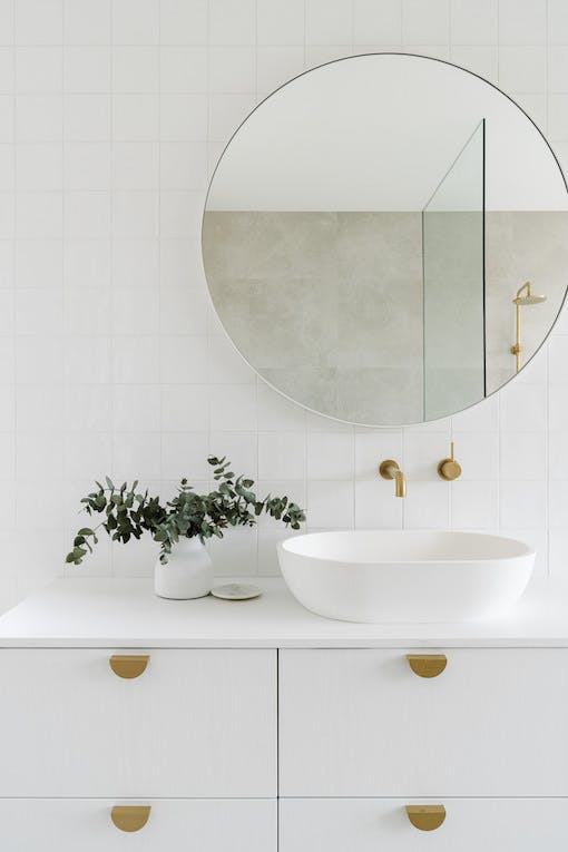 Evier de salle de bain immaculé et vasque et miroirs aux lignes rondes et épurés avec plante grasse.
